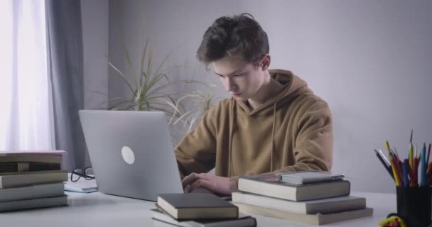Diligent Caucasian college student closing laptop and sighing. Portrait of genius brunette boy sitting at the table with homework. Lifestyle, education, intelligence. Cinema 4k ProRes HQ. - Кадры, видео