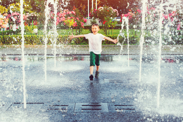 Happy boy running between water jets in city fountain. Summer in the city. Cute kid playing in a fountain with water. Child having fun in fountain. Summer vacation. Happy childhood. - Photo, Image