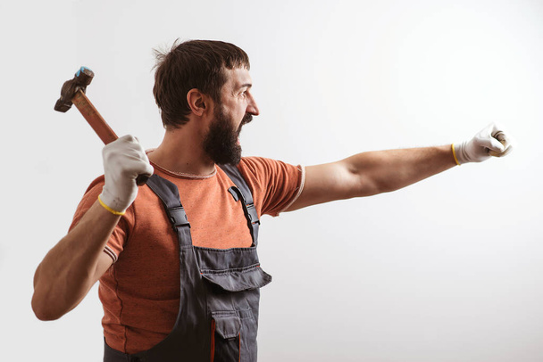 Baard bouwer werkt met hamer. Bouwer met professioneel gereedschap. Een schreeuwende voorman met een hamer. Brutale man aan het hameren. Bouwwerkzaamheden. - Foto, afbeelding