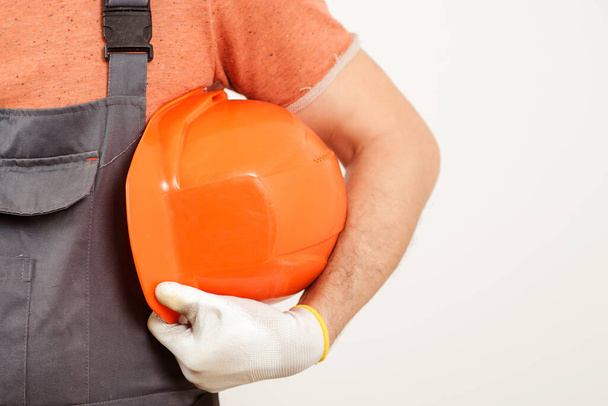 Workman holding orange helmet close up. Worker in a construction site. Builder wearing a protective glove. Safety helmet for contractor. Construction worker, tradesman or manual labourer. - Fotografie, Obrázek