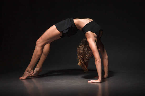 Young girl doing yoga on a black background - Фото, изображение