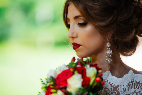 brunette bride in a dress with a wedding bouquet in the park on a background of greenery - Фото, изображение