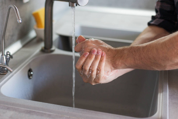a man washes his hands in the kitchen sink. Modern kitchen - Фото, изображение