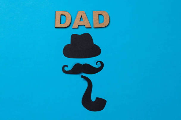 "Dad", word made from wooden letters, black hat, mustache, pipe and red hearts made of paper on blue background - Fotó, kép