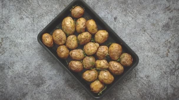 Oven gebakken hele aardappelen met kruiden en kruiden in metalen dienblad. Geroosterde aardappelen in jasjes. - Video