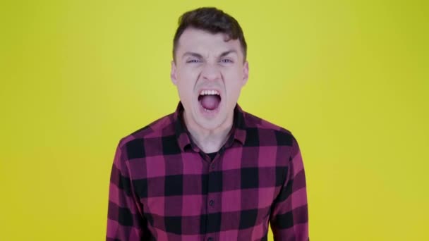 Boze man in een roze geruite shirt schreeuwt in de camera op een gele achtergrond - Video