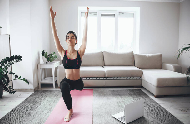 Mooie vrouw stretching haar spieren voor yoga les thuis tijdens de quarantaine met een laptop - Foto, afbeelding