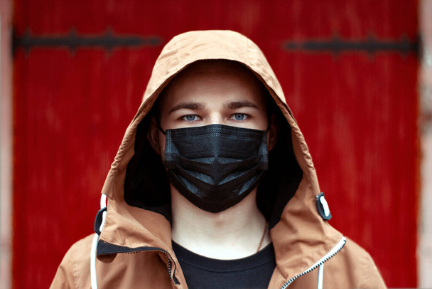Coronavirus karantinası. Koruyucu maske takan genç Avrupalı bir adamın portresi. Siyah tıbbi maskeli bir adam salgın hastalıktan dolayı, kırmızı arka planda. Tehlike durumu. Hava kirliliği 2019-NCov - Fotoğraf, Görsel