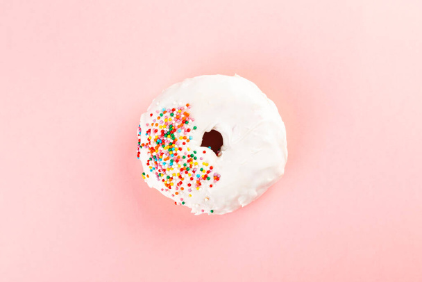 Donut with white icing and multicolored sugar pastry topping on pink background. Top view - Foto, imagen