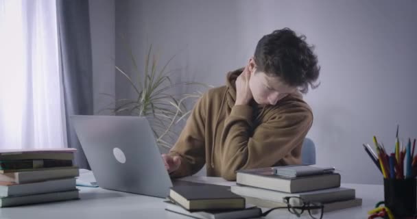 Brunette Caucasian boy moving stiff neck as sitting at the table with laptop. Portrait of male college student having tech neck symptom. Health care problems, sedentary lifestyle. Cinema 4k ProRes HQ. - Imágenes, Vídeo