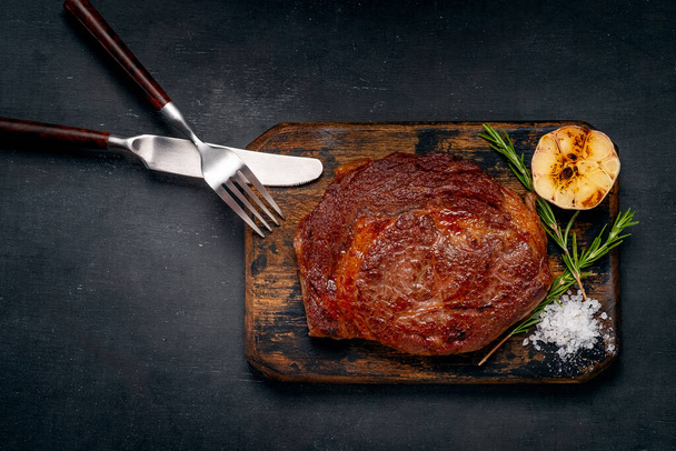 Grilovaný hovězí steak na dřevěné desce na tmavém pozadí, servírující masové pokrmy - Fotografie, Obrázek