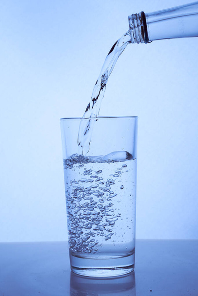Свежая чистая вода наливается из бутылки в стакан. Светлый фон
. - Фото, изображение
