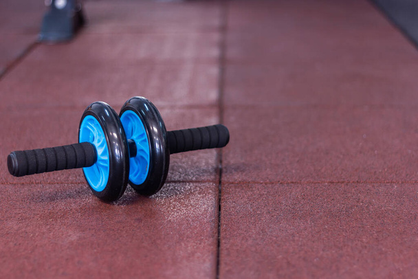 μπλε και μαύρο γυμναστήριο κοιλιακό τροχό σε κόκκινο καουτσούκ - Φωτογραφία, εικόνα
