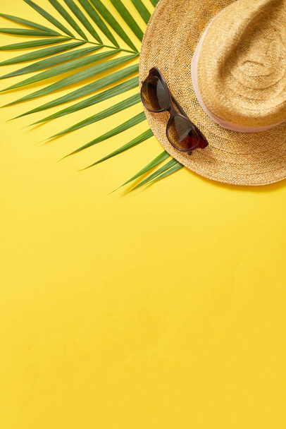 Strohhut, grünes Palmblatt und Sonnenbrille vor gelbem Hintergrund. Sommerkonzept. Flache Lage, Draufsicht - Foto, Bild