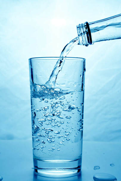 agua limpia fresca se vierte de una botella en una taza de vidrio. Fondo claro
. - Foto, imagen