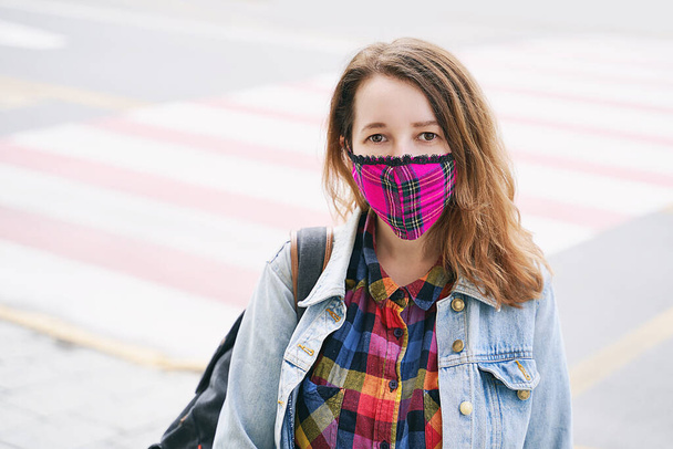 Young woman wearing a plaid handmade face mask and colorful shirt standing on the street. - Fotografie, Obrázek