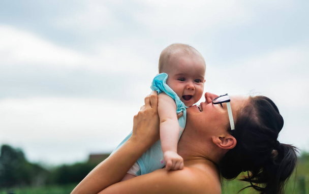 Un disparo de madre cariñosa sosteniendo al bebé al aire libre. Concepto de crianza con espacio de copia a la izquierda
 - Foto, Imagen