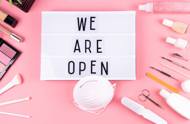 "We 're Open "sign for barber shop and hair salon, after quarantine, on pink background with face mask, hand disanitizer, makeup, nail polish, makeup brushes and nail set.Reopening concept
.  - Фото, изображение