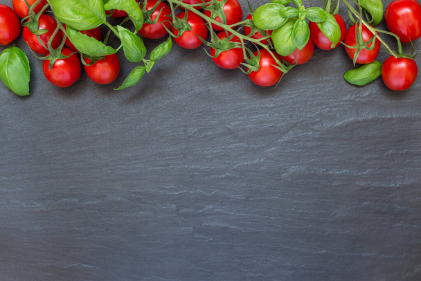 Tomates cereja com folhas de manjericão no fundo de ardósia escura, horizontal, vista superior, espaço de cópia
 - Foto, Imagem