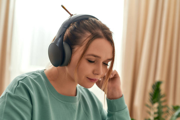 Happy beautiful woman in headphones with closed eyes listening music or studying language online, enjoying e-learning at home. Close up portrait - Photo, Image