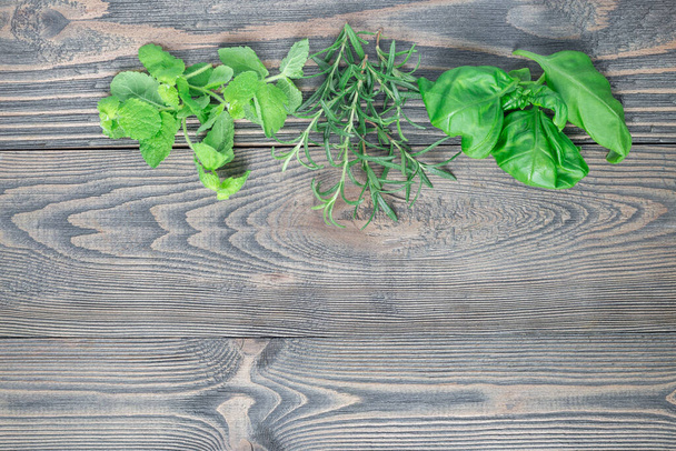 Basil, mint, rosemary. Fresh green herbs laying on wooden background, top view, horizontal, copy space - Foto, imagen