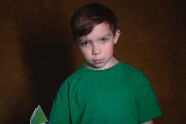 Porträt eines neunjährigen blonden Jungen in grünem T-Shirt auf braunem Hintergrund - Foto, Bild