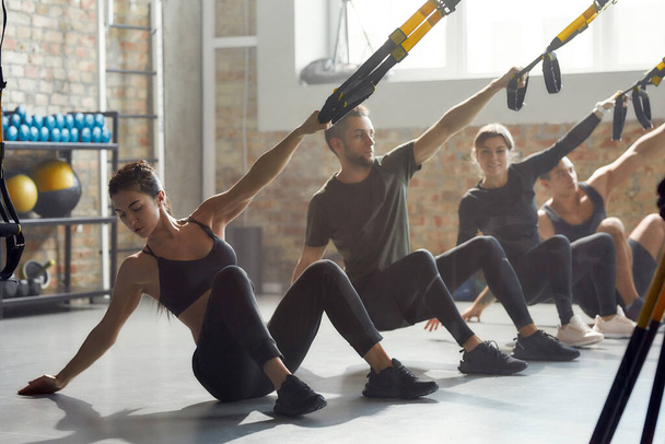 Fitness Together. Full-length shot of men and women doing fitness TRX training exercises at industrial gym. Push-up, group workout concept - Fotografie, Obrázek