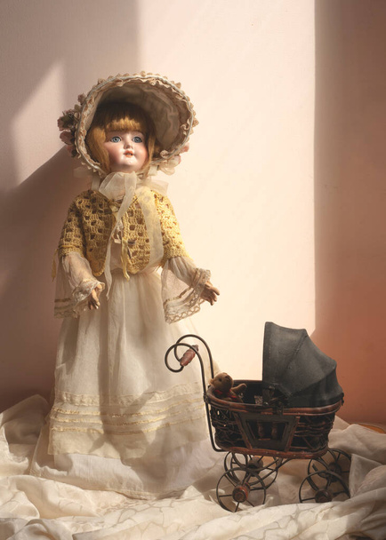 Маленькая фарфоровая статуя мальчика, стоящего с коляской, старинной куклой, антиквариатом
 - Фото, изображение