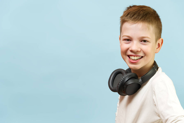 Smiling young handsome boy on a blue background in headphones. concept of baby radio, dj, singer or karaoke. happiness be music everywhere. - Foto, immagini