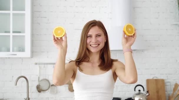A cheerful girl covers her eyes with orange slices. Emotions in the white kitchen. Healthy eating. - Filmagem, Vídeo