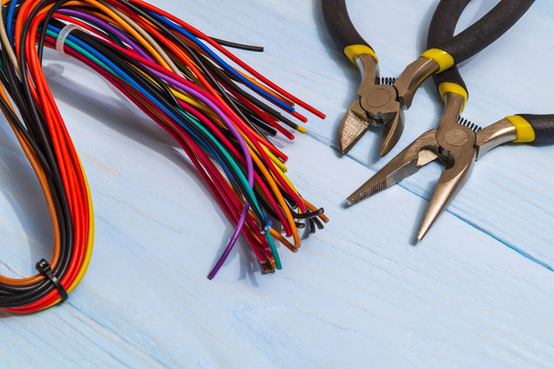 Alicates herramienta y cables multicolores para electricista primer plano en tableros azules
 - Foto, Imagen