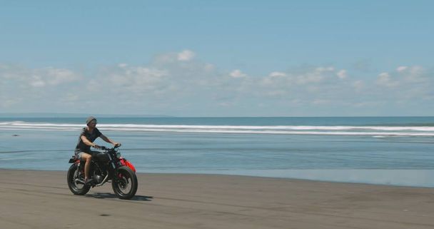 Motorcyclist driving his motorbike on the beach - 写真・画像