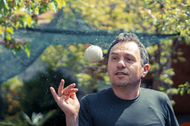 Man in his forties throws and spins a ball that makes water spirals on a green background - Photo, Image