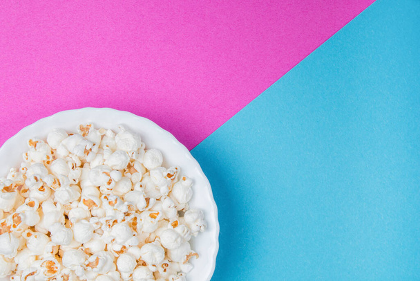Witte kom popcorn op een blauwe en paarse achtergrond - Foto, afbeelding