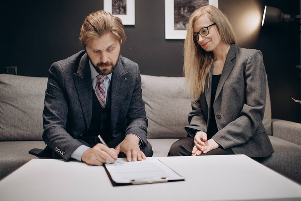 Kaksi liikekumppania allekirjoittaa asiakirjoja toimistossa
 - Valokuva, kuva