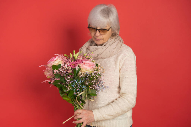 Glückliche Seniorin mit Blumenstrauß auf farbigem Hintergrund - Foto, Bild