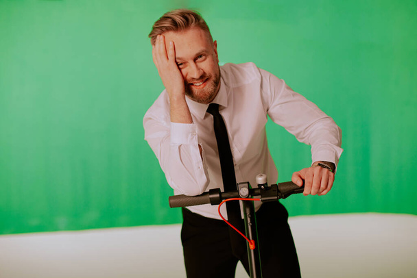 Homem barbudo com scooter elétrico, imagem em um fundo de estúdio verde
 - Foto, Imagem