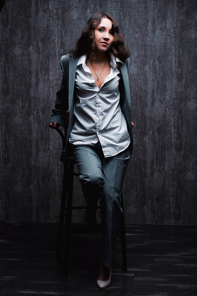 Beautiful girl in a suit and a man's shirt in the Studio on a chair beautiful emotions - Foto, afbeelding