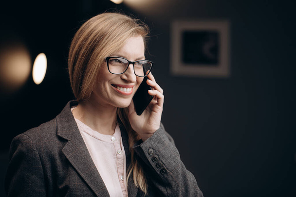 Mujer feliz hablando en el teléfono inteligente en la oficina moderna
 - Foto, imagen