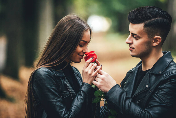 Close up portrait of lovely stylish man and woman dating in autumn park, she smells a rose that he gives her. - Foto, Imagem
