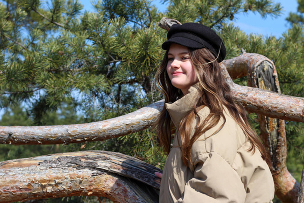 Ağaç gövdesinde kabarık ceketli ve şapkalı bir kız. Ağaçta gülümseyen genç - Fotoğraf, Görsel