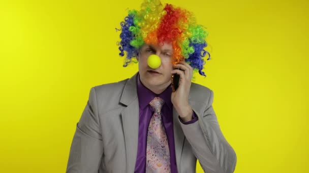 Clown businessman entrepreneur boss talking on mobile phone. Yellow background - Footage, Video