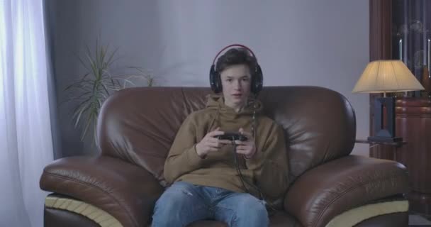 Portrait of satisfied Caucasian boy winning in video game. Cheerful teenage gamer resting at home in armchair with game console. Gaming, lifestyle, leisure, joy. Cinema 4k ProRes HQ. - Séquence, vidéo