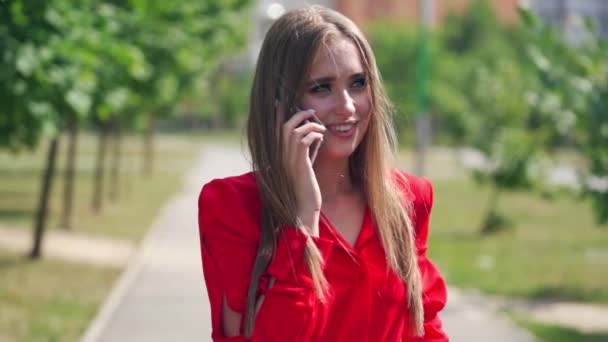 Young woman talking on the phone. Portrait of a beautiful lady with long hair holding a mobile phone on the blurred city background. Slow motion. - Filmagem, Vídeo