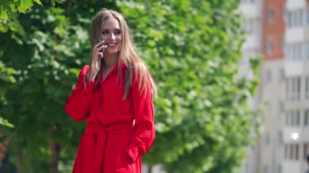 Gorgeous young lady with mobile phone. Beautiful woman with long hair talking on the phone happily. Pretty girl standing near the green tree. Slow motion. - Кадри, відео