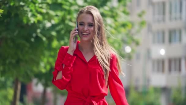 Happy woman talking on the cellphone. Attractive smiling young lady in red dress walking in the city and talks on the mobile phone. Slow motion. - 映像、動画