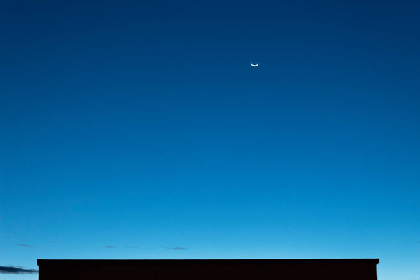 Atemberaubender Sonnenuntergang Waning creacent moon in Verbindung mit Quecksilber und Jupiter Planet zu blauer Stunde ohne Wolken Himmel. - Foto, Bild