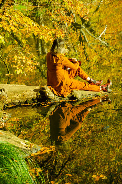 blonde hair female model dressed in orange, sitting by the lake - Photo, Image