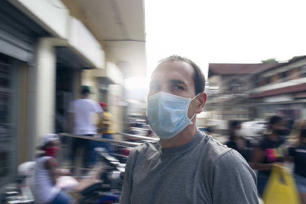 a young dominican man wearing protective mask in street surrounded by people back to normal life - Photo, Image