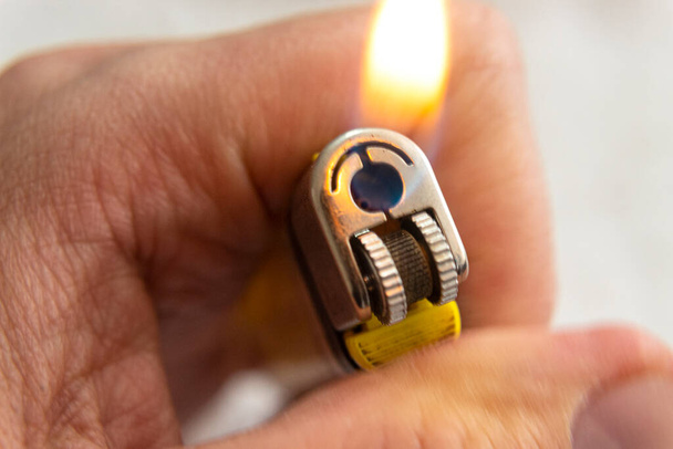 Close-up van een mannelijke hand met een gele aansteker met vlam op witte achtergrond - Foto, afbeelding